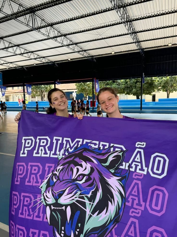 Duas alunas segurando bandeira roxa do primeirão com ilustração de tigre