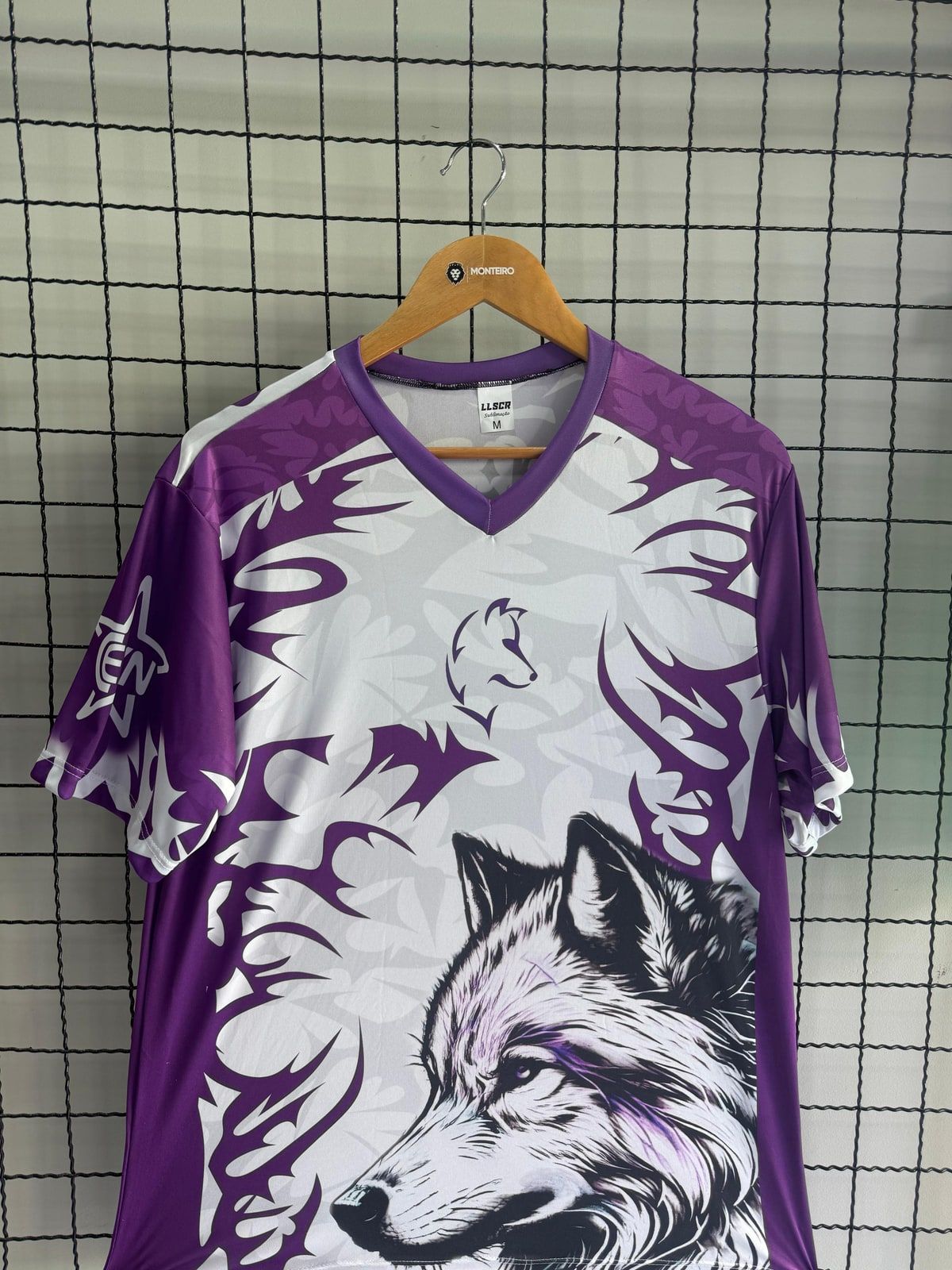 Camisa esportiva roxa e branca com estampa de lobo, pendurada na loja