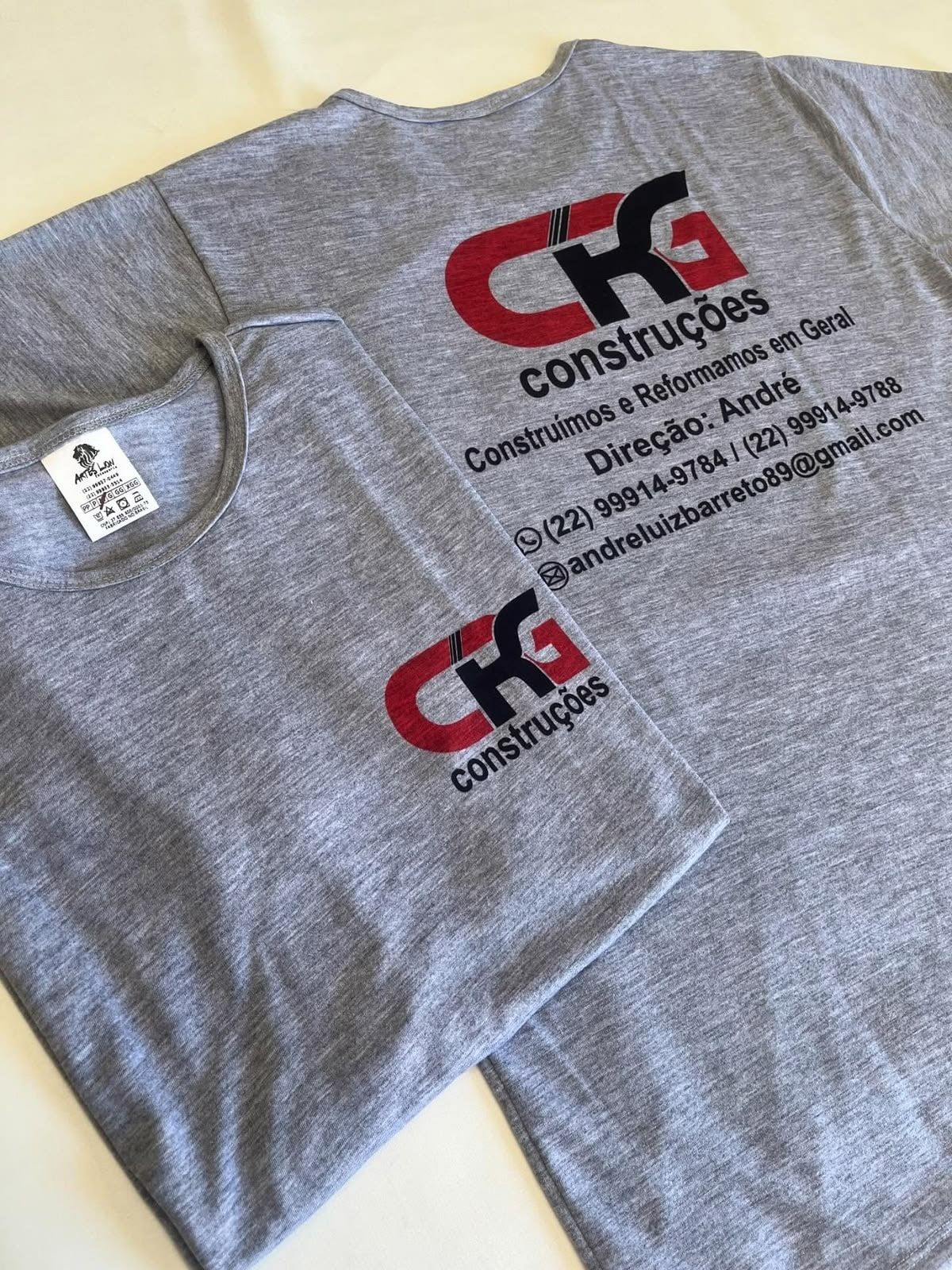 Camisetas cinza com logo de construtora e contatos impressos nas costas