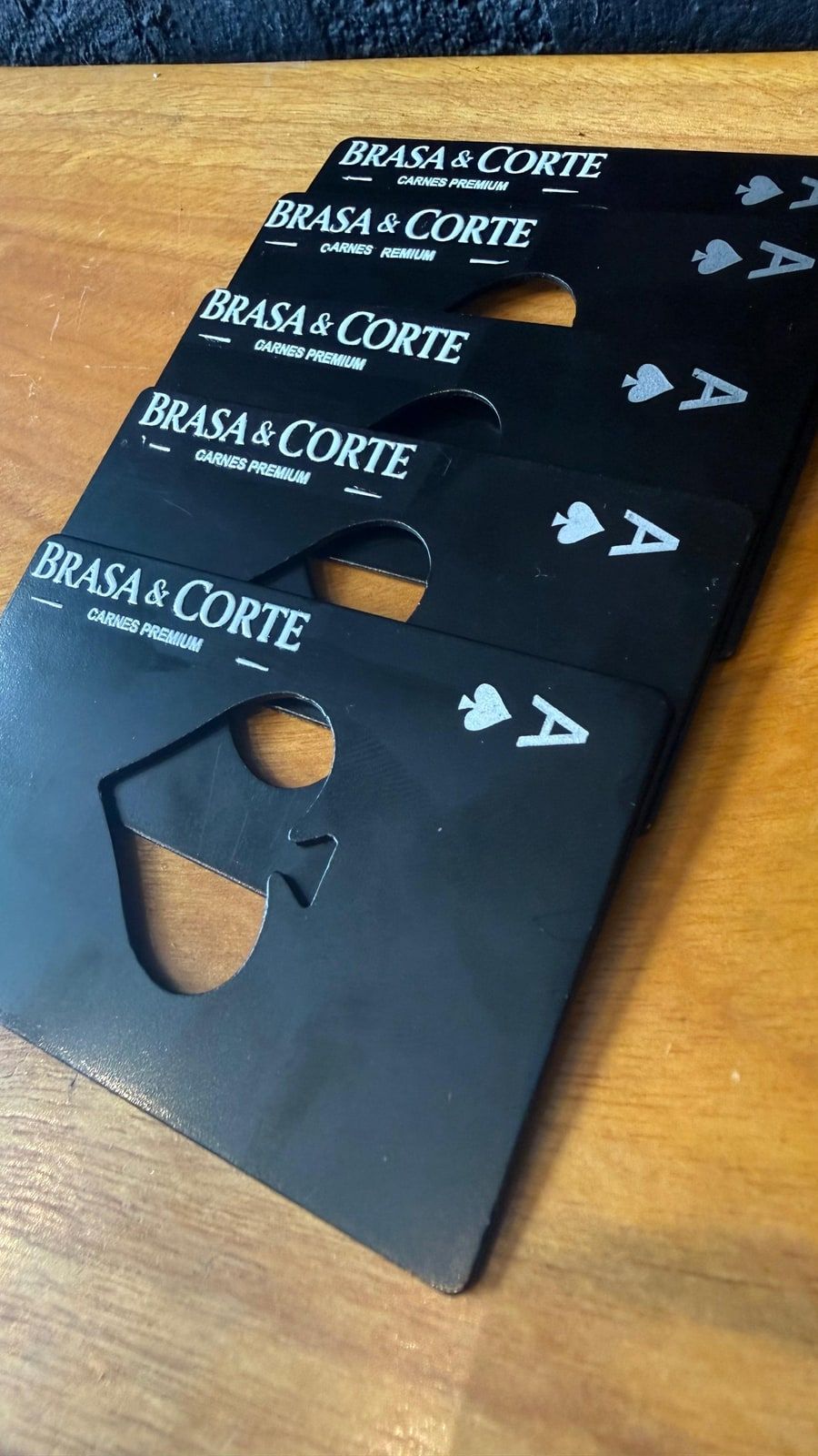 Peças pretas recortadas com a marca Brasa & Corte e um ás de espadas vazado